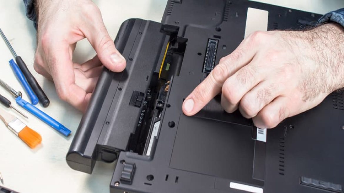 Laptop service. Removal of the battery by a service technician. Tools lie on the table.